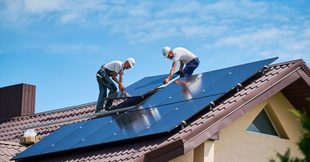 Deux ouvriers installent des panneaux solaires sur le toit d'une maison 